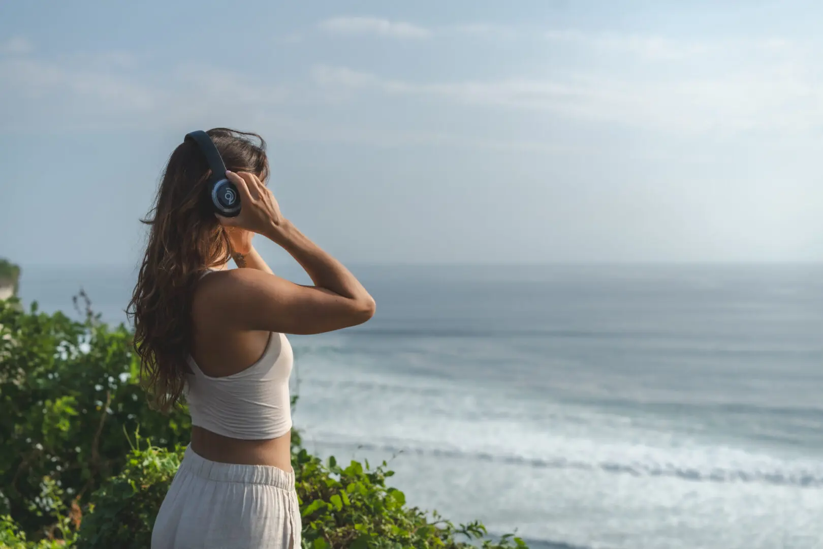 A woman standing on top of a hill near the ocean.